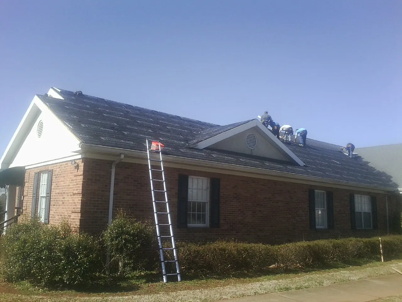Crew tearing shingles off a brick ranch roof with a ladder set — Emergency Roof Repair work by our crew in Rocky Hill