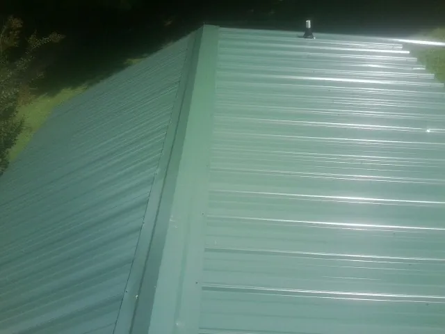 New green metal panels meeting at the ridge of a roof — Flat Roof Repair work by our crew in Rocky Hill