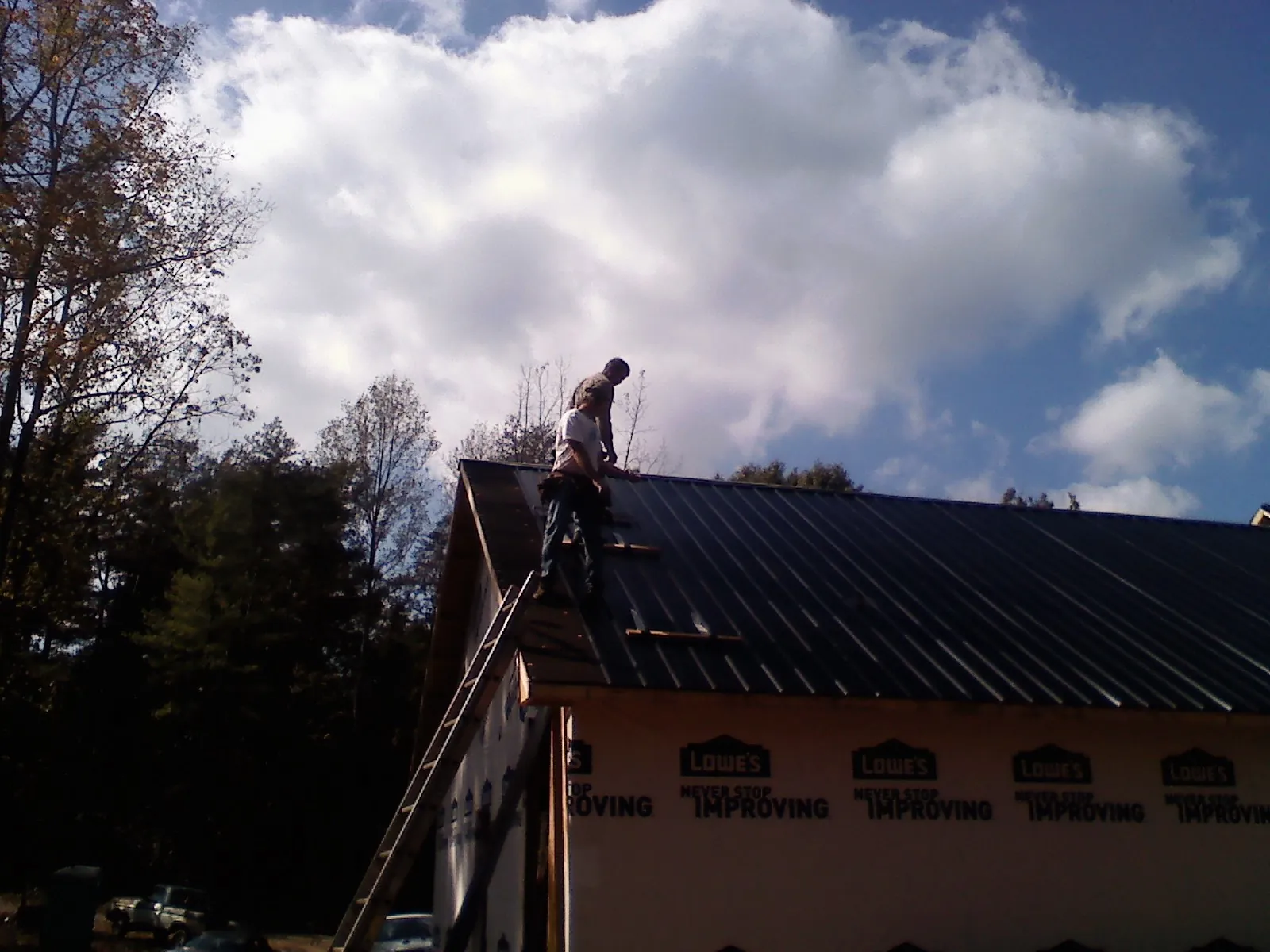 Roofer fastening dark metal panels high against a cloudy sky, from a Roof Inspection job in Rocky Hill